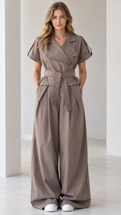Front full-length view of woman wearing taupe asymmetrical zip wide leg jumpsuit with tie belt