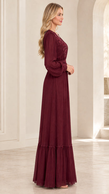 Side profile view of woman wearing burgundy floor-length long sleeve gown