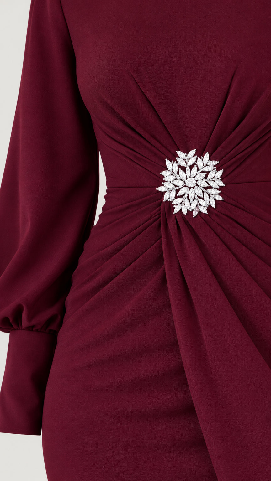 Close-up of gathered waist and floral-style embellishment on burgundy dress